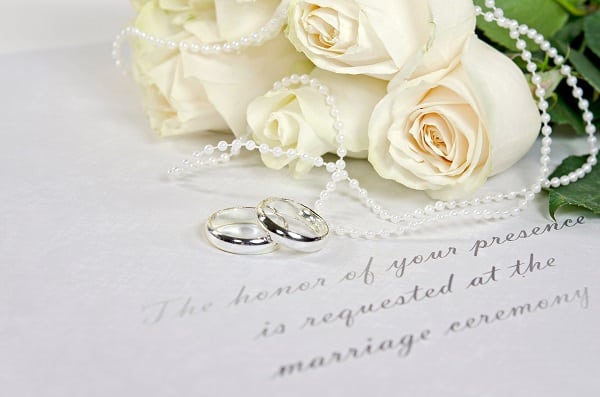 white roses and rings on wedding invitation